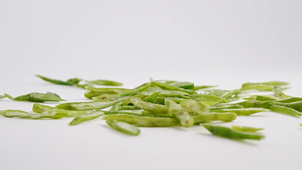 Locate the pod wall before the defined cooked assessment Obliquely cut green bean pieces expose pod walls and some seeds on a white surface