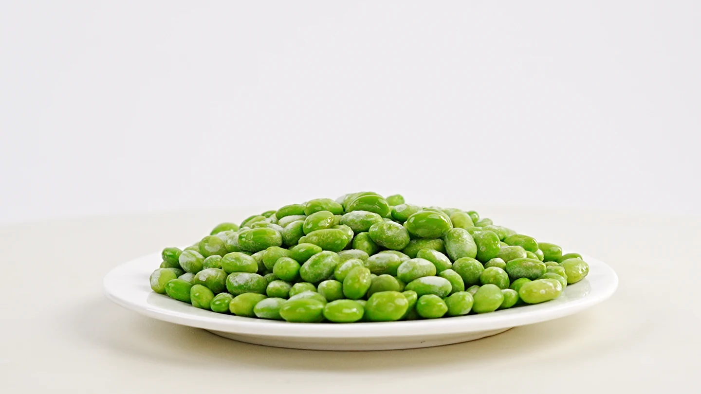 Shelled green edamame beans on a plain plate identify the ingredient form discussed before the holding comparison.