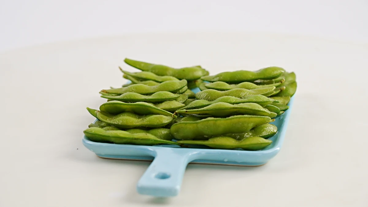 Edamame in its green pod form Green edamame pods arranged on a small blue serving board