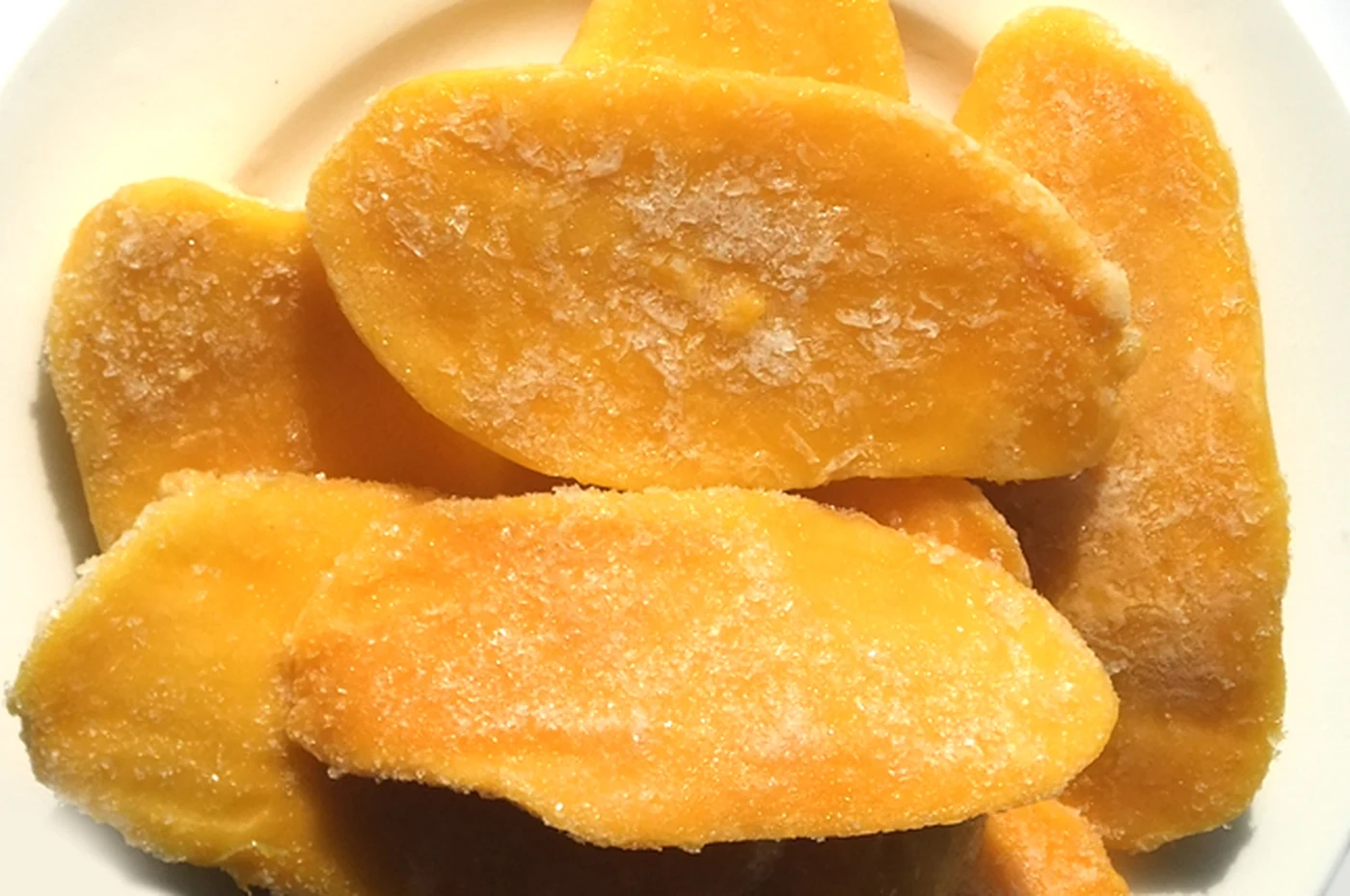 Frosted mango cheeks on a plain plate, identifying a frozen fruit rather than fresh mango cargo